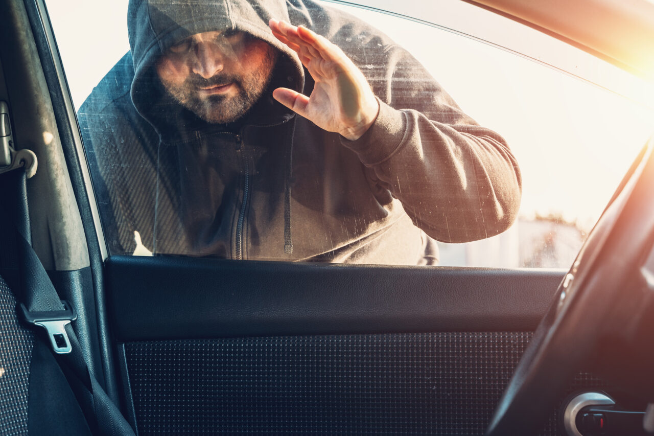 Car thief in hood looks inside car through window to show vehicle theft prevention