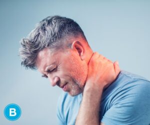 man wincing in pain while rubbing back of neck after apparent injury