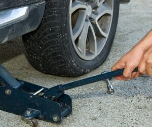 person's hand cranking tire jack and lifting vehicle