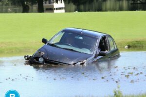 black car crashed and partially submerged in shallow pond