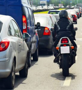 Motorcyclist rides along white line in heavy traffic.