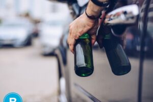Hand holding beer bottle out car window while vehicle is stopped.