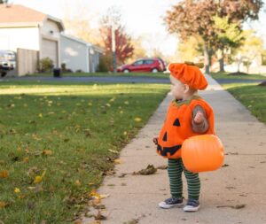 small child dressed as jack-o-lantern stands on sidwalk while trick-or-treating