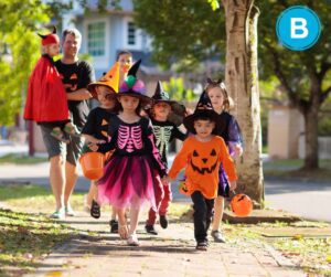 group of children trick-or-treating in costume with parent. Group is walking down neighborhood sidewalk.