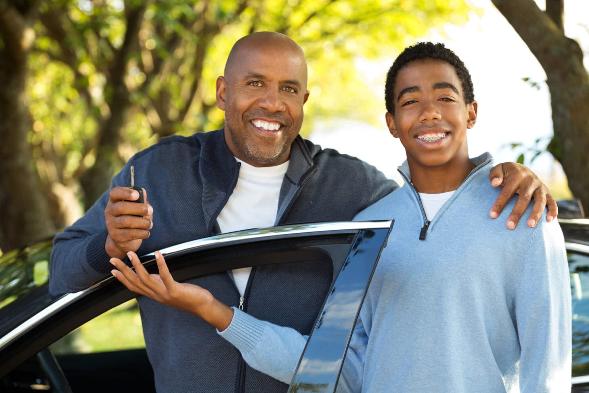 African American father holding keys and preparing to teach his teen son how to drive.
