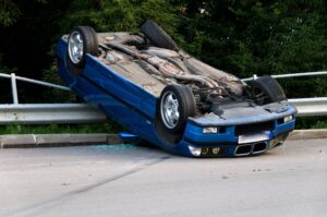 blue car flipped upside down against guard rail after accident