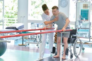man stands holding onto bars in rehabilitation center while being supported by medical attendant