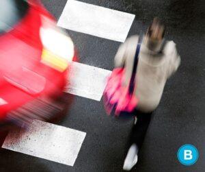 woman crossing crosswalk with red car turning and getting ready to hit her