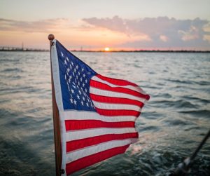 American flag on boat out on water with sunset in distance