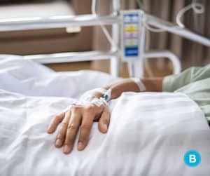 man's arm with IV, in hospital bed