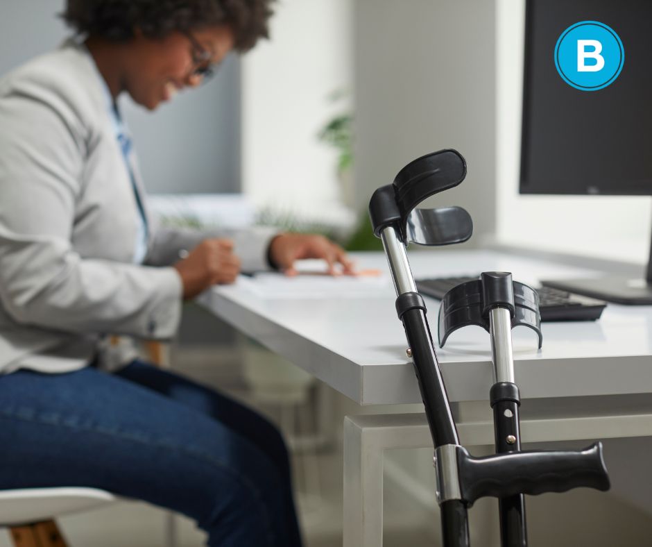 woman of color sitting at computer desk, with crutches propped beside her.