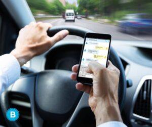man using phone to text while behind wheel and driving
