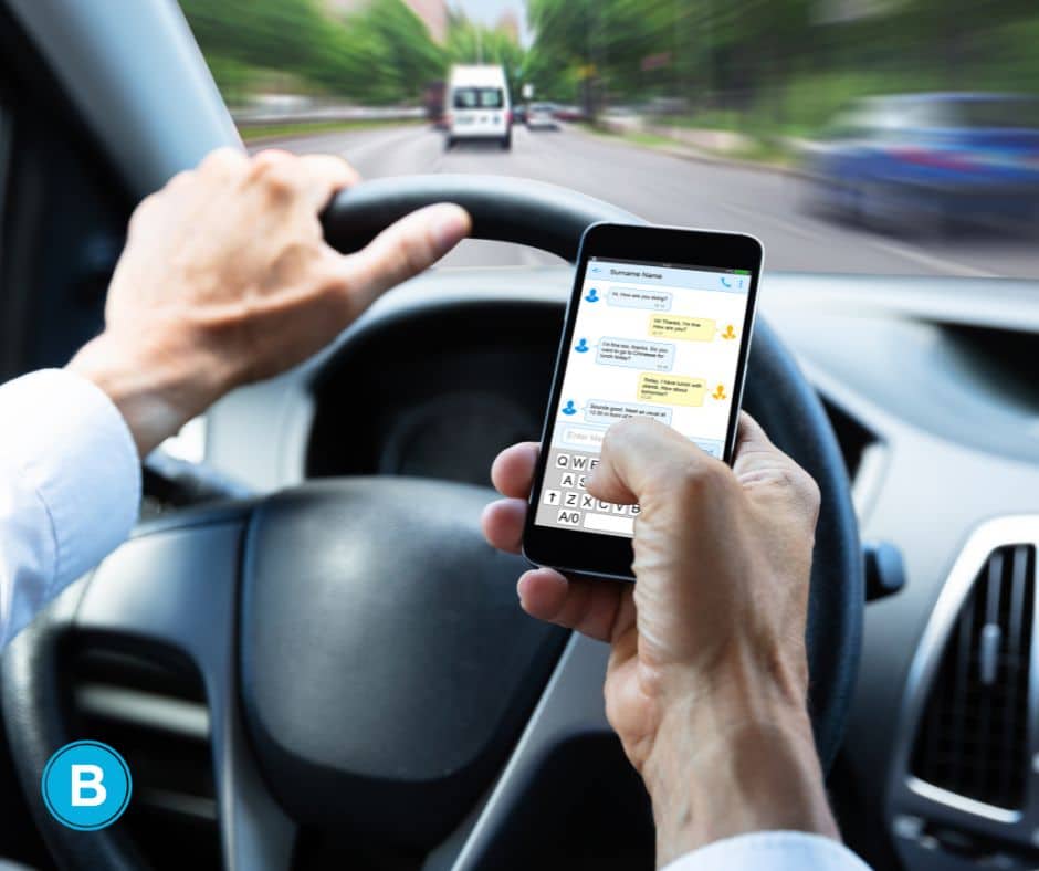 man using phone to text while behind wheel and driving