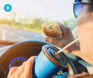 woman eating and drinking while behind wheel and driving car