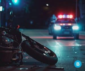 motorcycle laying on side on road in dark with police car lights flashing in distance while approaching