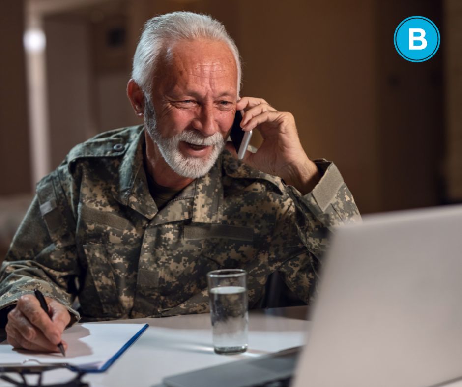 elderly veteran speaking on phone while working on a laptop