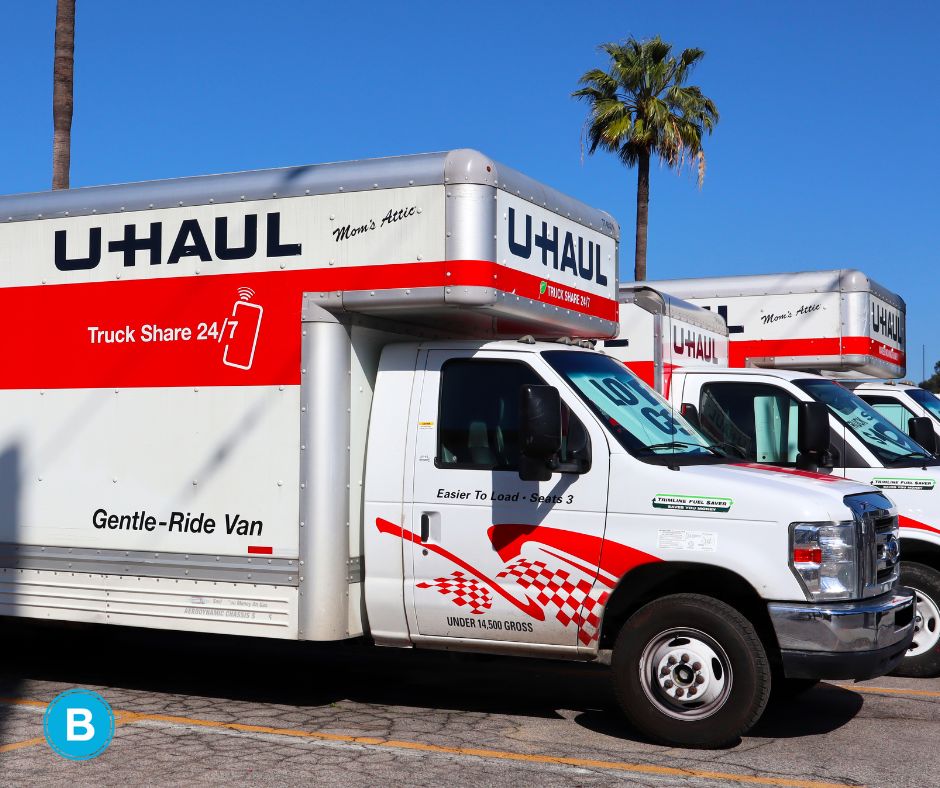 A U-Haul moving truck parked in a lot with blue skies and palm trees behind.