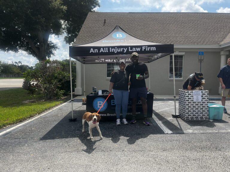 Two people with a beagle on a leash at the Brooks Law Group tent during the pet adoption event in Winter Haven