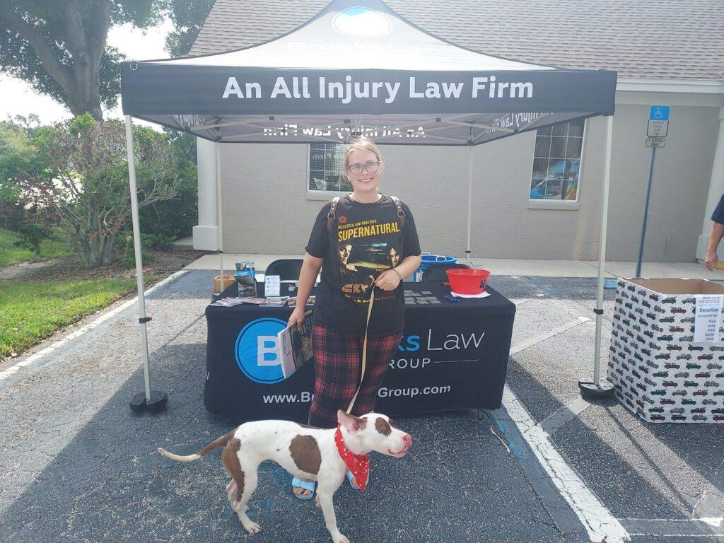 A woman with a brown-and-white dog in a red bandana at the Brooks Law Group tent during the pet adoption event