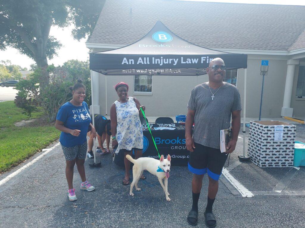 Three people with a white dog on a green leash outside the Brooks Law Group office during the pet adoption event